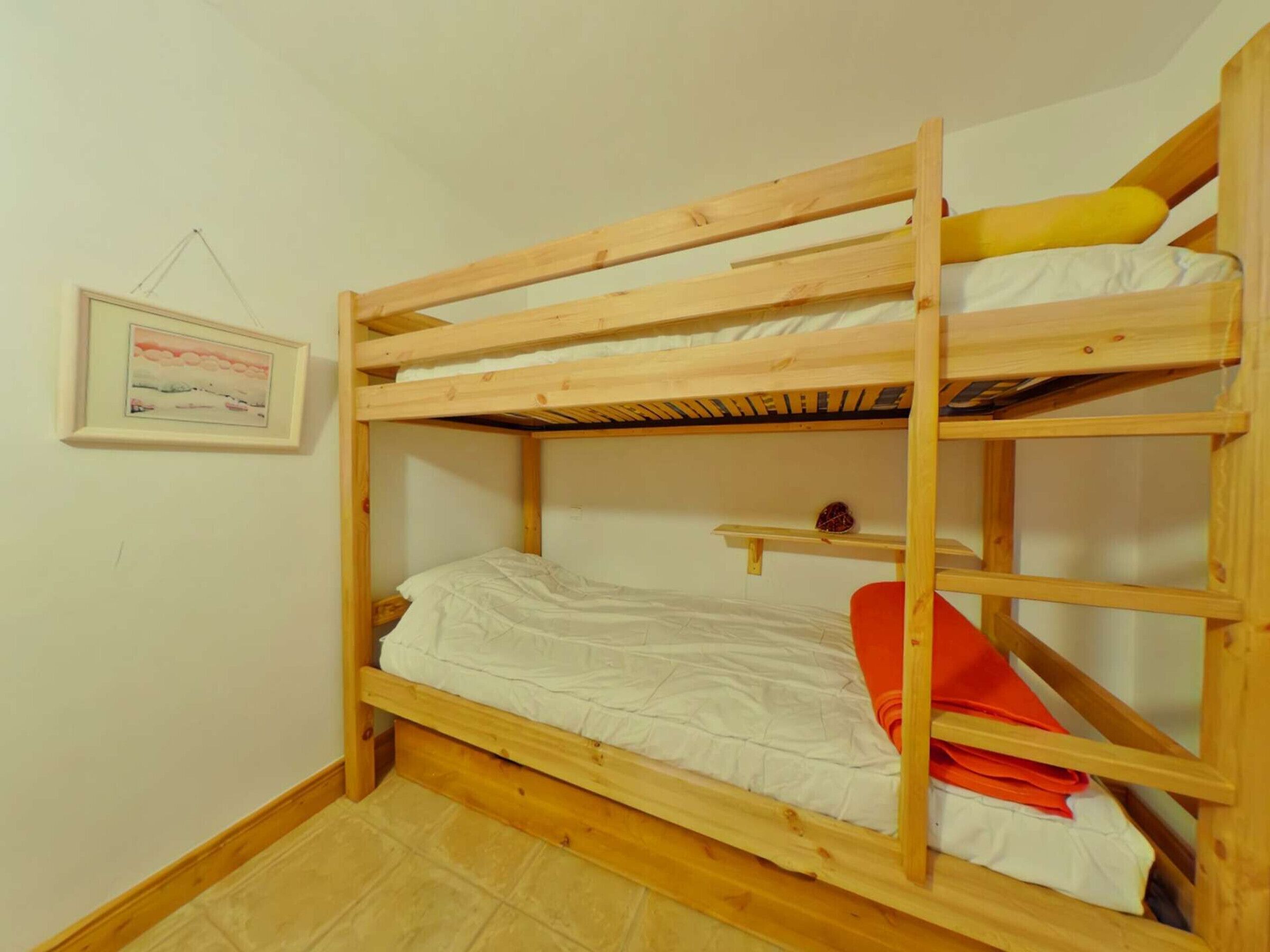 A bunk bed with a wooden frame, white bedding, and a small shelf with a picture frame and a small item on it.