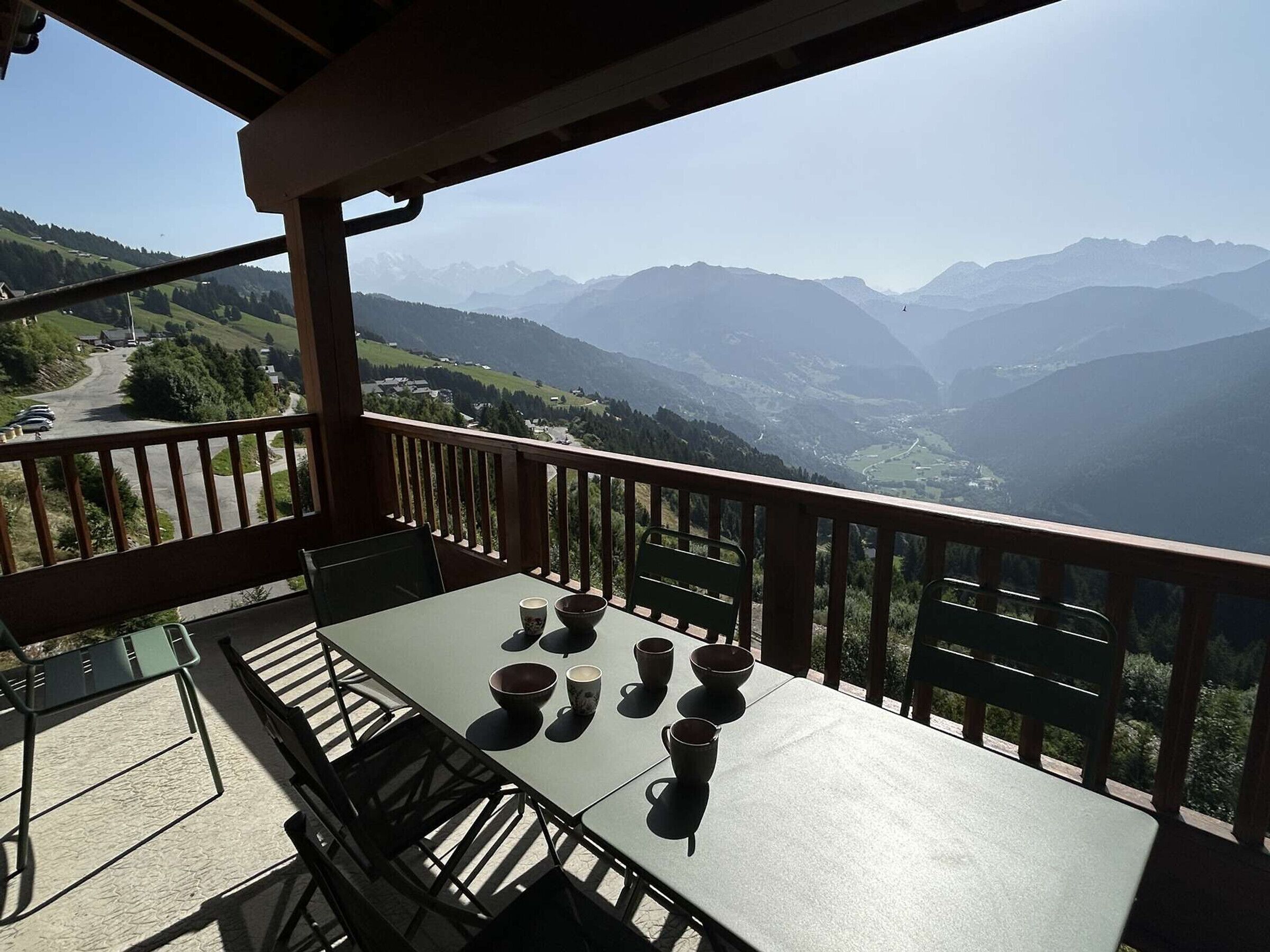 A balcony with a table set for four, overlooking a mountainous landscape.