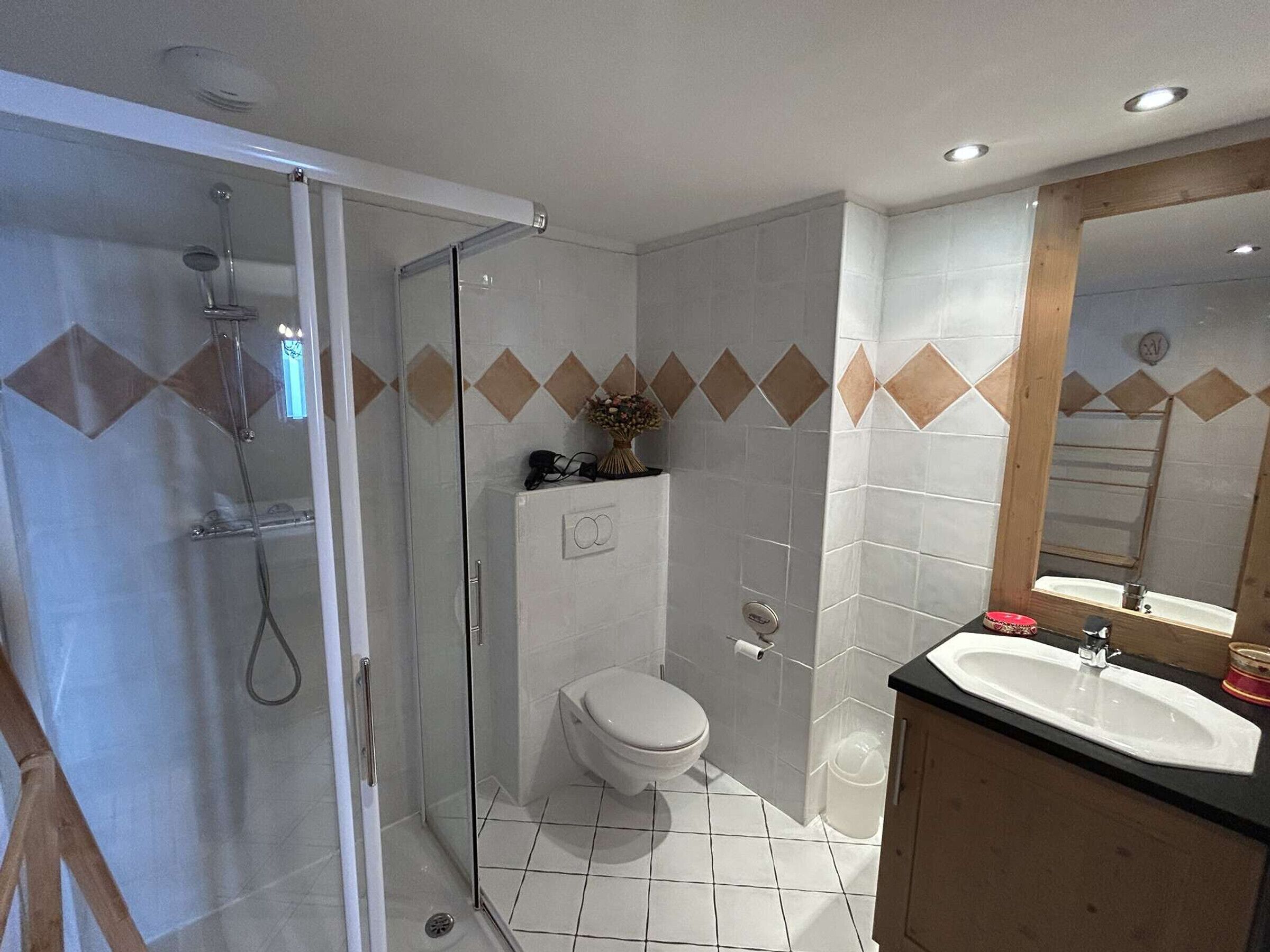 Un baño con ducha envuelta en vidrio, inodoro, lavamanos y espejo.