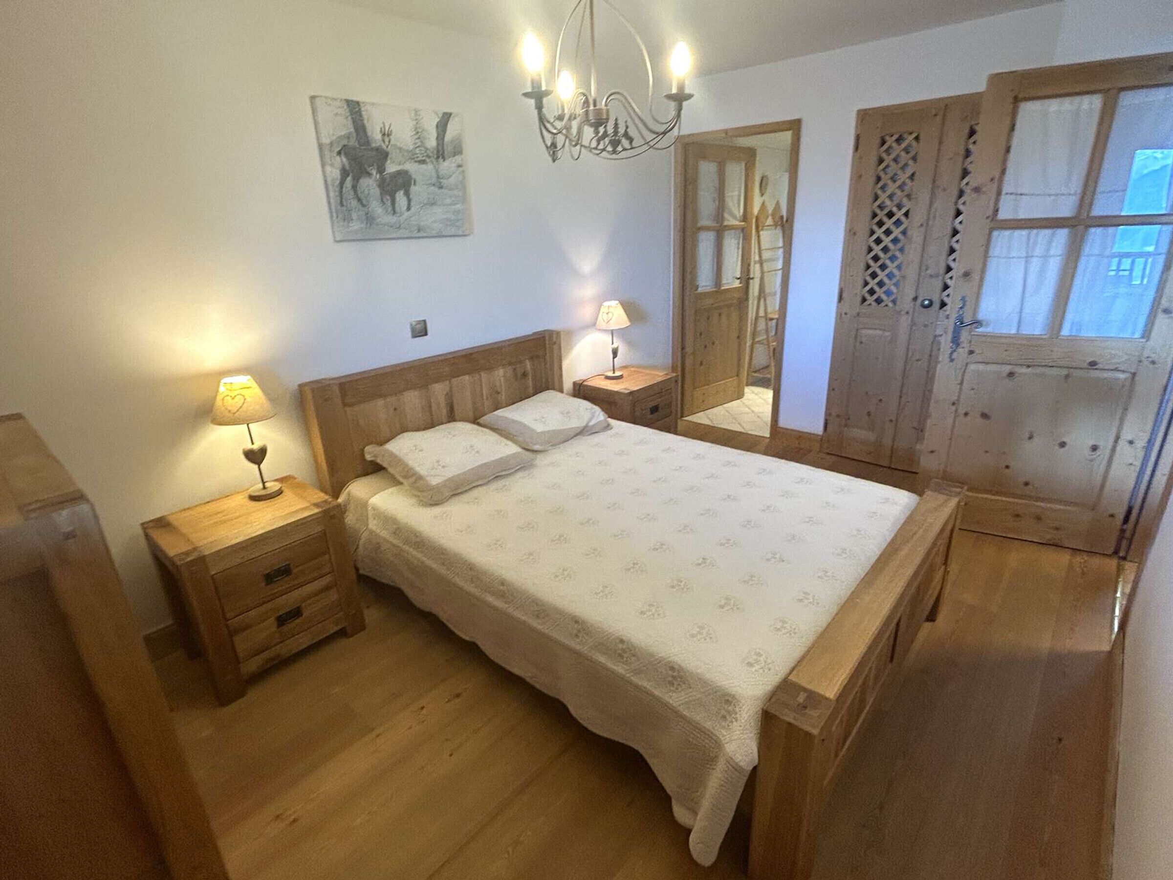 A bedroom with a wooden bed, bedside tables, a chandelier, a painting, and a wooden wardrobe.