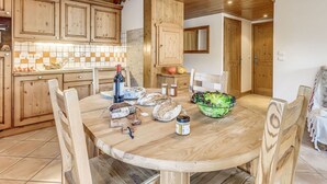 A wooden dining table with chairs, a bottle of wine, a loaf of bread, and a bowl of salad in a kitchen with wooden cabinets and a tiled backsplash. - Champagny en Vanoise, Apt 6 people, 2 bd, Parking, Balcony (Champagny-en-Vanoise)