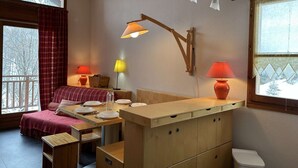 A cozy room with a wooden bed, a small table with plates and a lamp, and a window with curtains. - Duplex chalet 6-8 ppl, garage, WiFi, Montgenèvre (Montgenèvre)