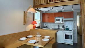 A compact kitchen with wooden cabinets, a microwave, a stove, and a dining area with a table set for four. - Duplex chalet 6-8 ppl, garage, WiFi, Montgenèvre (Montgenèvre)
