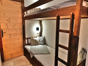 A bunk bed with a ladder, a small bedside table, and a wall-mounted light fixture.