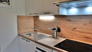 A compact kitchen with white cabinets, a stainless steel sink, a wooden backsplash, and a black induction cooktop.