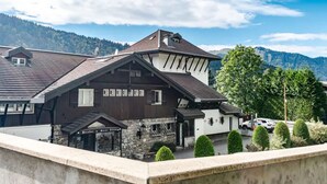 A chalet-style building with a stone facade and multiple windows, set against a mountainous backdrop.