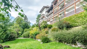 A multi-story building with balconies, surrounded by lush greenery and a well-maintained garden.