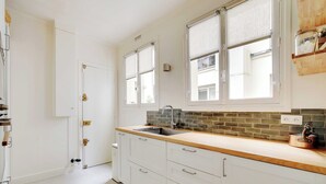 A kitchen with white cabinets, a wooden countertop, a sink, and a window with a view of the outside. - Elegant Apt 2bdr- Arc de Triomphe / Champs-elysees (Paris)