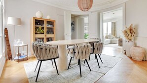 A dining area with a large table, upholstered chairs, a chandelier, and a bookshelf. - Elegant Apt 2bdr- Arc de Triomphe / Champs-elysees (Paris)