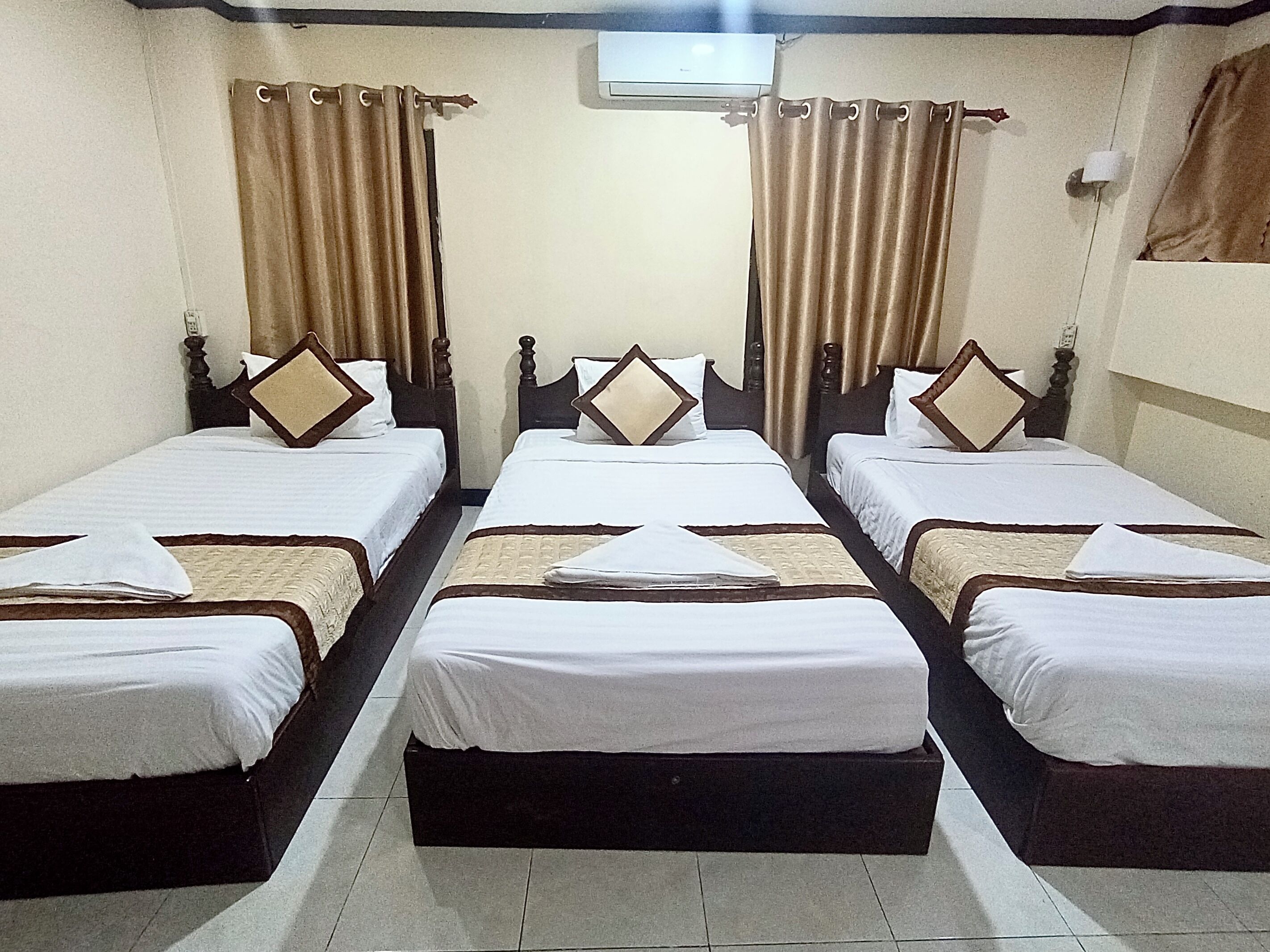 Habitación de hotel con cuatro camas individuales alineadas, cada una con cabecero de madera y ropa de cama blanca.