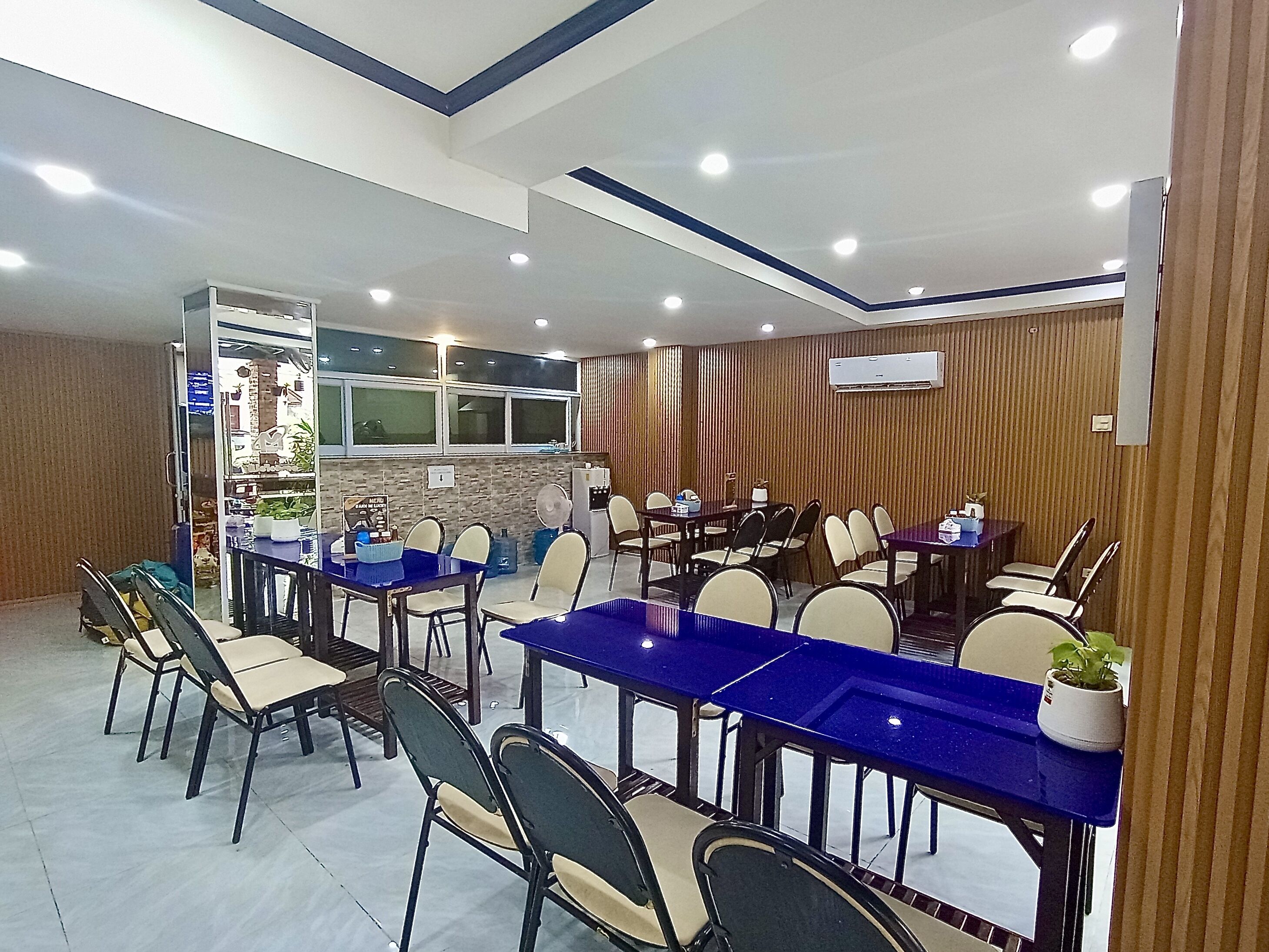 A conference room with multiple tables and chairs, a kitchenette, and an air conditioning unit on the wall.