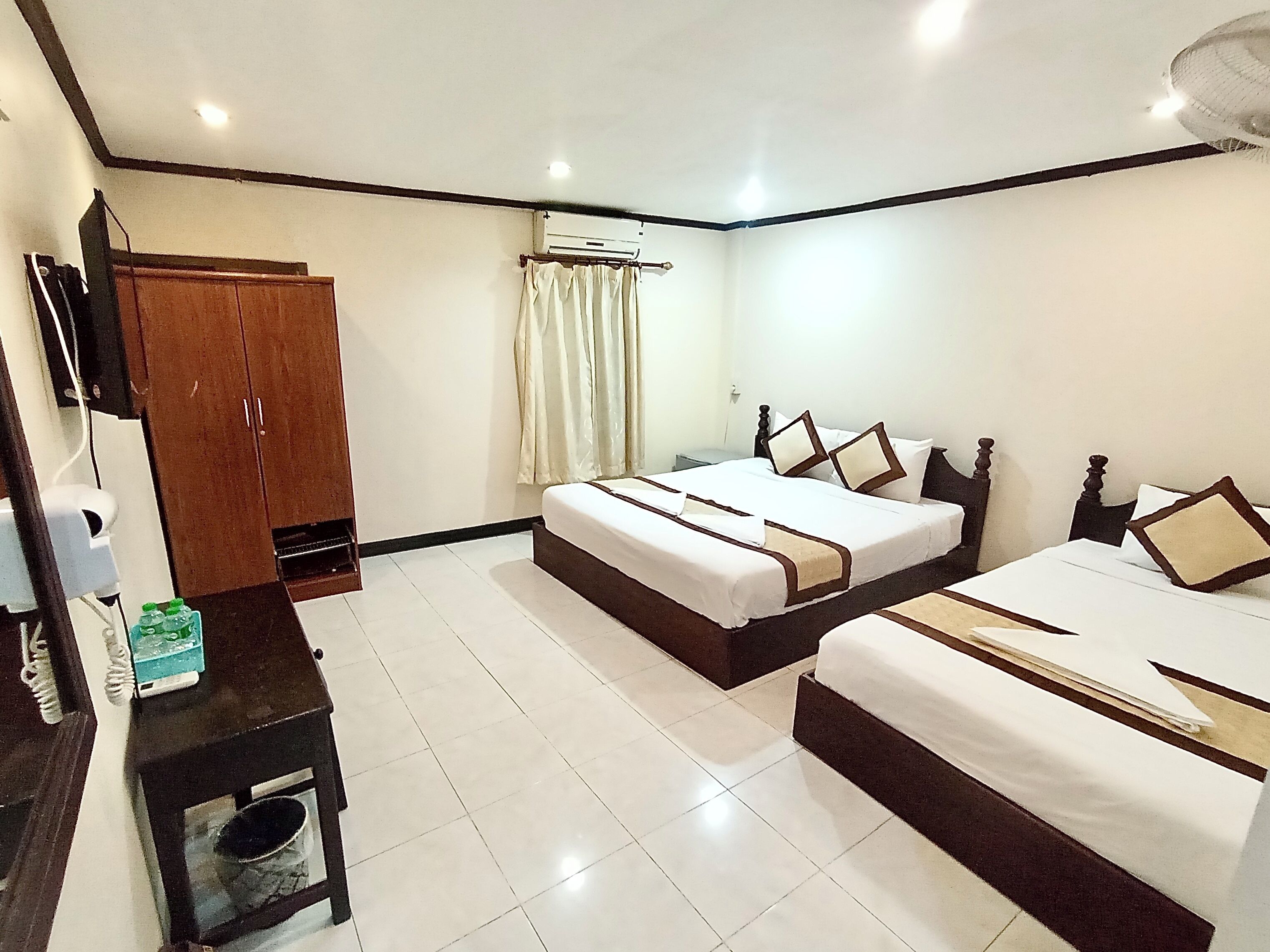 A hotel room with two beds, a wardrobe, a desk with a chair, and a television.