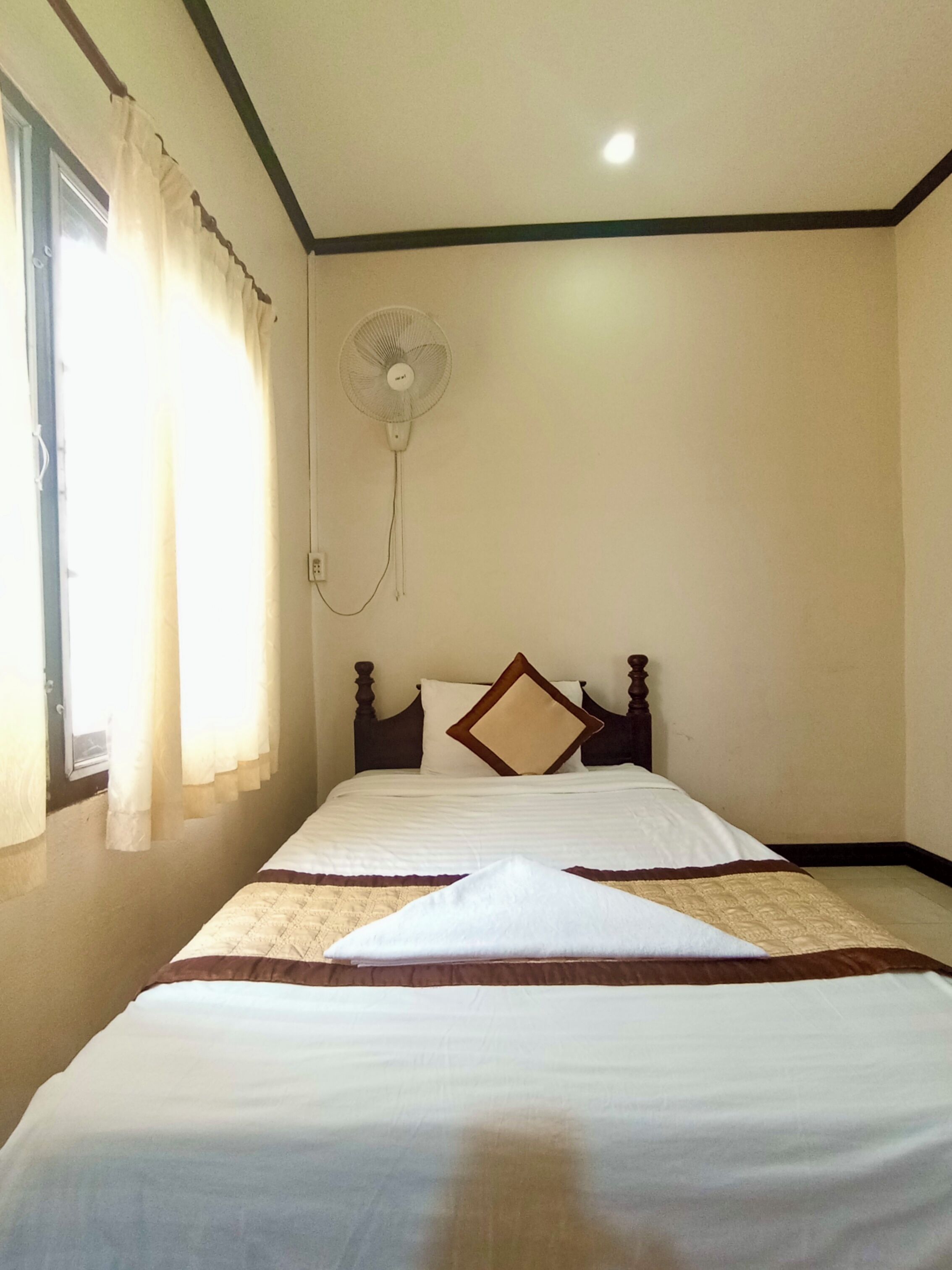 A room with a bed, a standing fan, and a window with curtains.