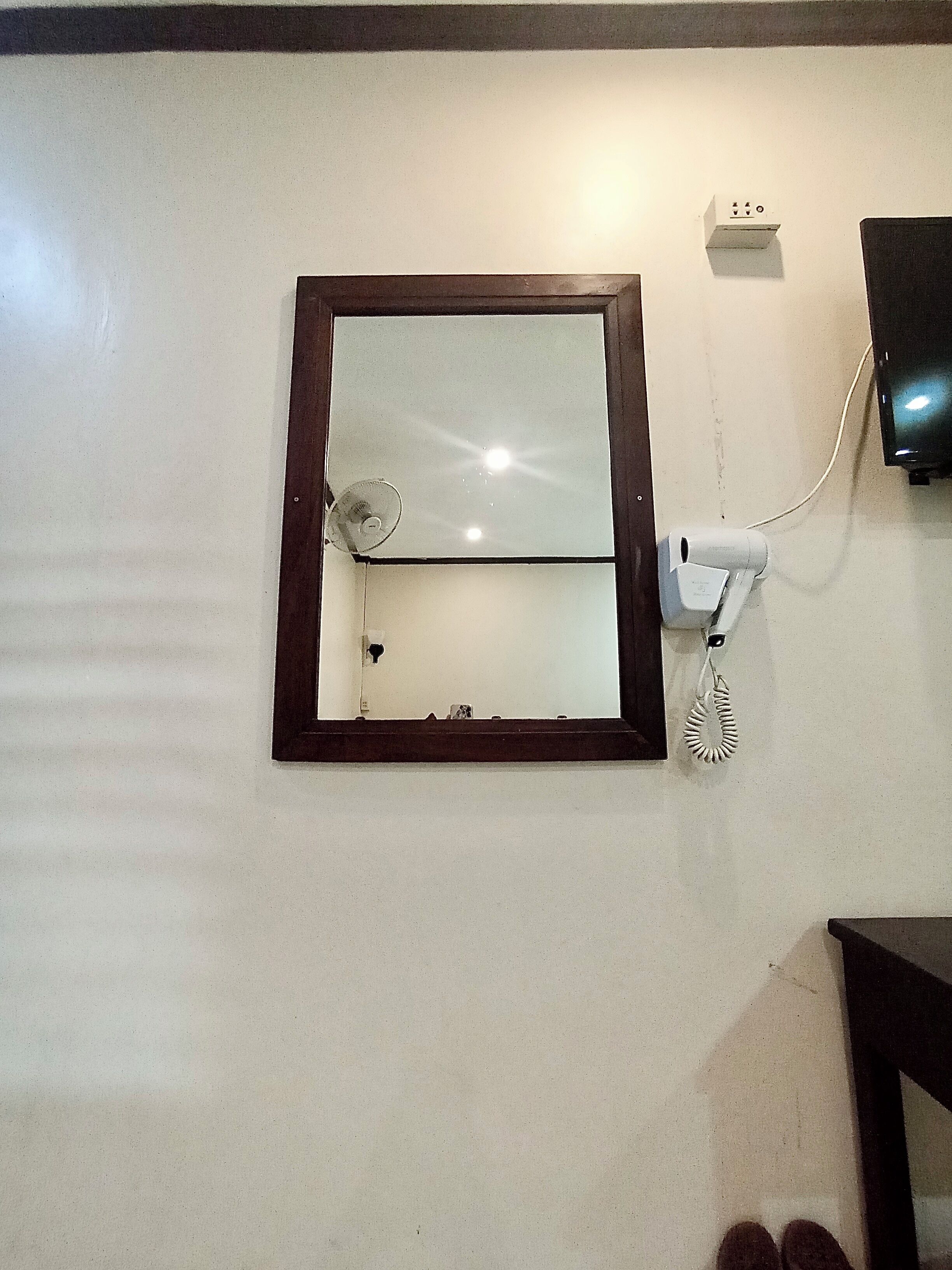 Un miroir avec un cadre en bois, accroché au mur, un sèche-cheveux et un téléviseur fixé au-dessus.