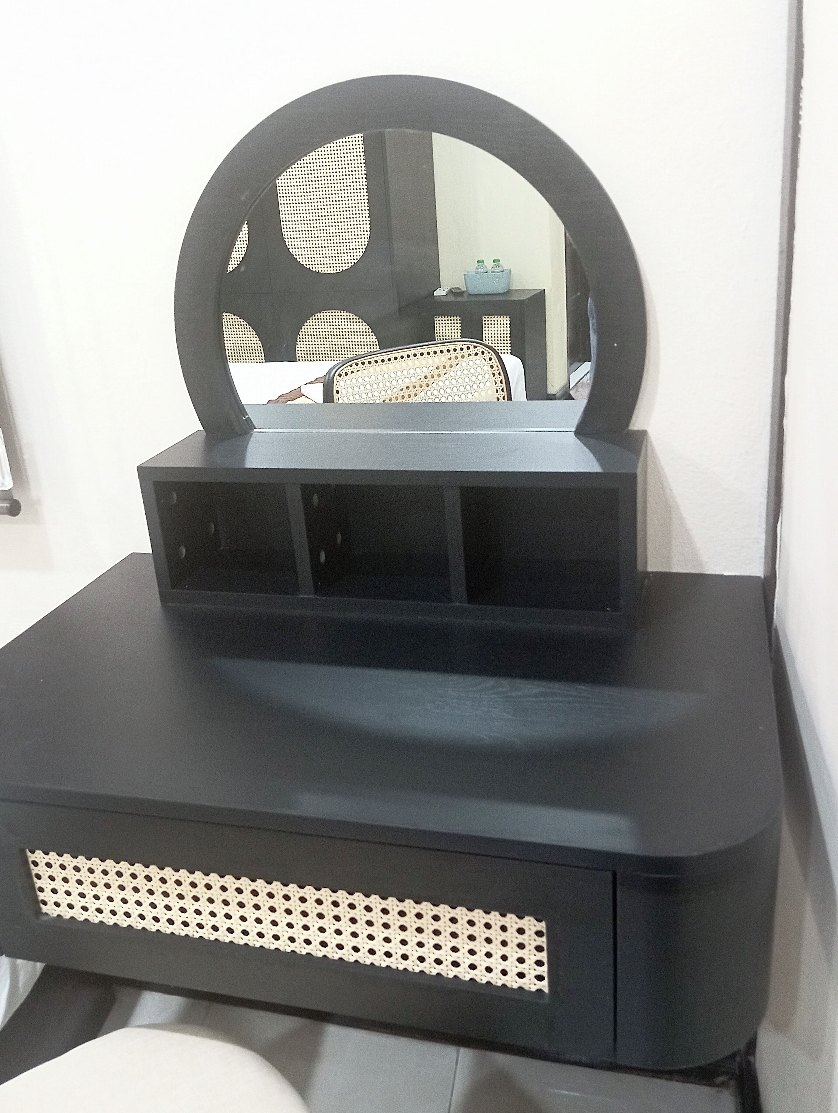 A black vanity with a round mirror, a small shelf, and a perforated panel.