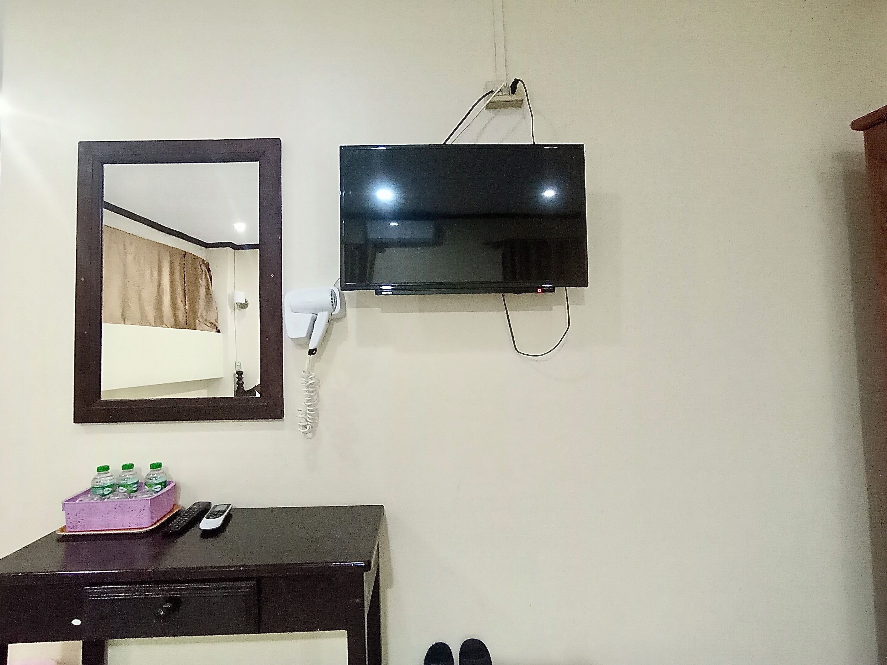 A room with a bed, a TV mounted on the wall, a mirror, a dresser, and a pair of shoes.