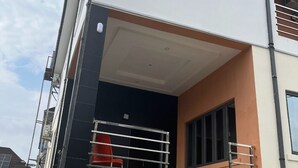 A modern two-story building with a balcony, a red chair, and an air conditioning unit. - R-Oak Hotels and Apartments  (Abuja)