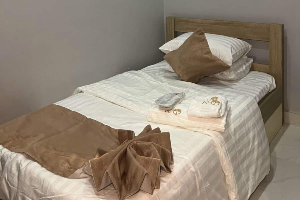 A single bed with a wooden headboard, white bedding, and a brown throw blanket.