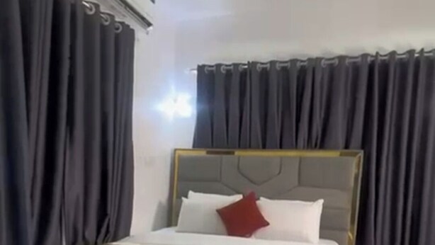 A modern bedroom with a large bed, dark curtains, and a minimalist design. - R-Oak Hotels and Apartments  (Abuja)