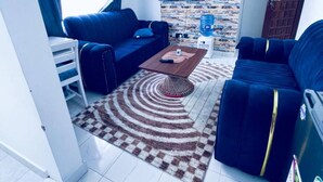 A compact living space with a sofa, a coffee table, a TV mounted on a textured wall, and a water dispenser. - Classy One bed airbnb by Miss Omuts,pool (Nairobi)