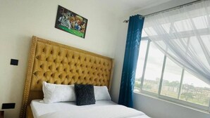 A hotel room with a large bed, a headboard, a window with curtains, and a wall-mounted picture. - Classy One bed airbnb by Miss Omuts,pool (Nairobi)