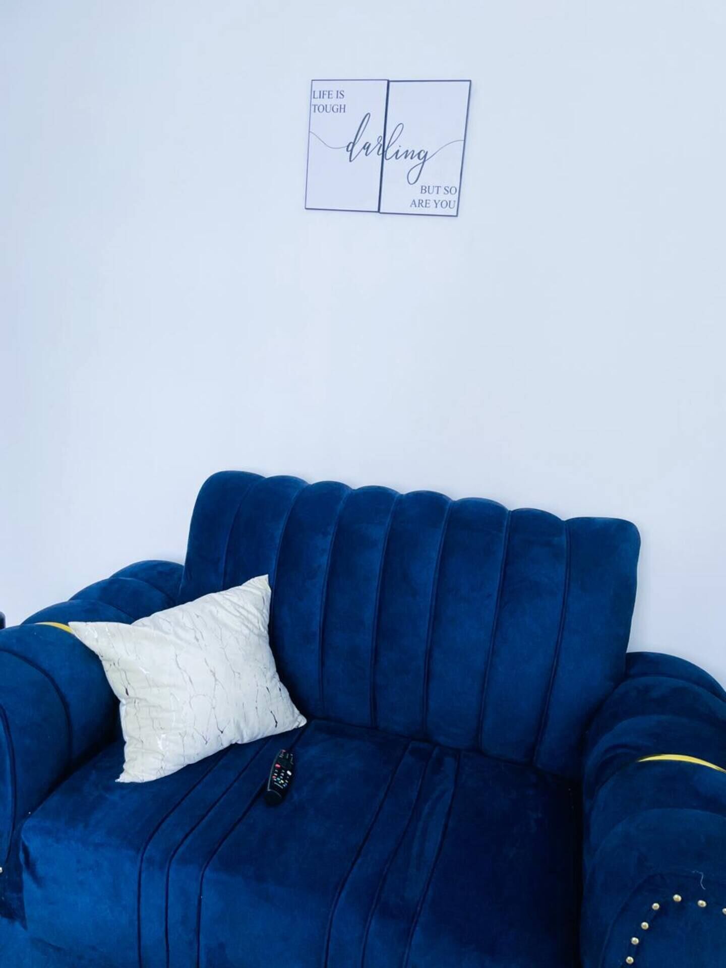 A blue sofa with a white pillow and a remote control on it.