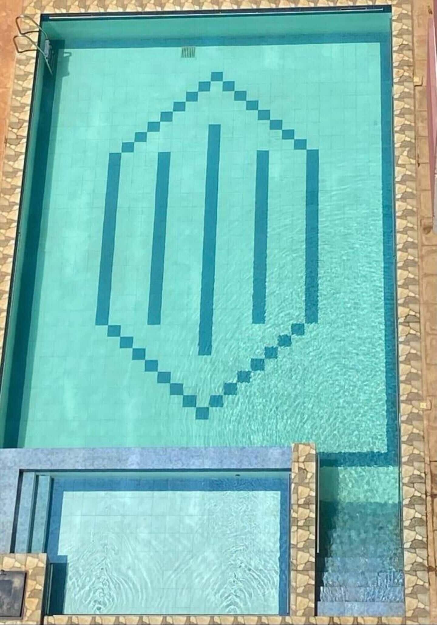 Une piscine dont le fond est recouvert de carreaux disposés selon un motif géométrique et qui est agrémentée d’une bordure décorative.