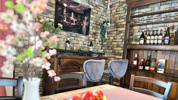 Interno di un ristorante con parete in mattoni, una zona bar con bottiglie e un tavolo con un piatto di mele.