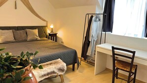 Una camera da letto con un letto, comodino, lampada, appendiabiti, scrivania, sedia e una pianta in vaso.
