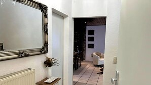 Un corridoio con un termosifone bianco, uno specchio decorativo e un vaso con piante essiccate.