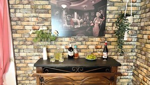 Angolo bar con parete in mattoni, un poster, un vaso con fiori, una bottiglia di liquore, una ciotola di uva e due sedie.