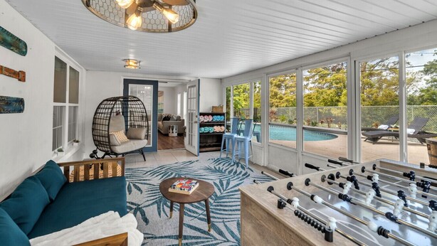 A spacious living area with a foosball table, a hanging chair, and a view of a backyard with a pool. - Modern 4BR Home w/ Private Heated Pool & Firepit (Seminole)