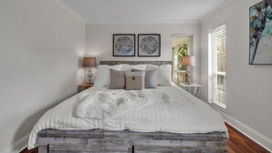 A bedroom with a bed, two bedside tables, a window with blinds, and two framed artworks on the wall. - Modern 4BR Home w/ Private Heated Pool & Firepit (Seminole)