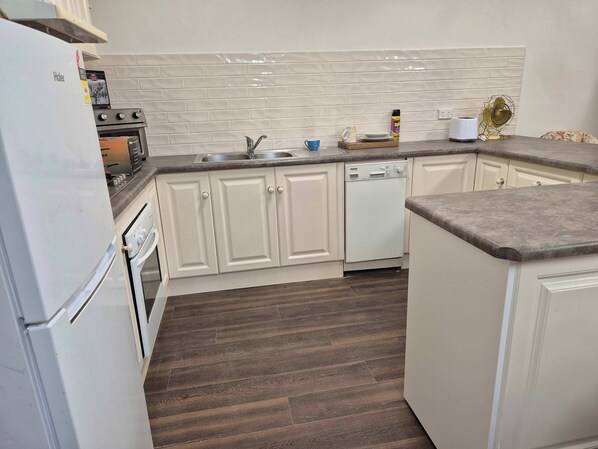 A kitchen with white cabinets, a dishwasher, a stove, and a sink. - Tipsy Hill Cottage, River Views at Walker Flat SA. Perfect for a weekend getaway (Forster)