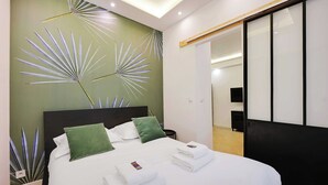 A neatly made bed with white linens and green pillows, a wall with a leaf pattern, and a wooden floor. - Serene Apartment - 1br/4p - Place de la Bastille (Paris)