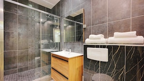 A modern bathroom with a glass shower enclosure, a wooden vanity, and a marble-tiled wall. - Serene Apartment - 1br/4p - Place de la Bastille (Paris)
