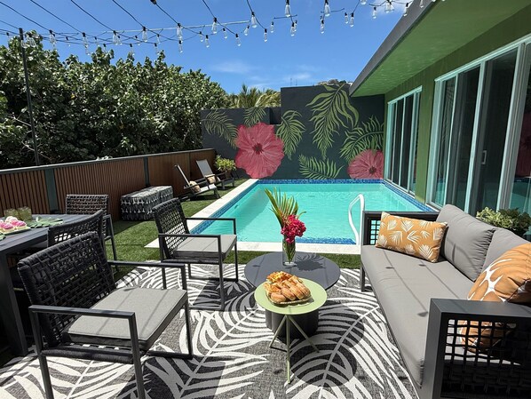 Un espace aménagé au bord de la piscine, comprenant une piscine, des chaises longues, une table à manger et un canapé.