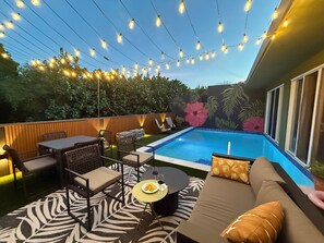 Un espace aménagé au bord de la piscine, comprenant une piscine, des chaises longues, une table à manger et des guirlandes lumineuses.