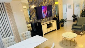 Een moderne woonkamer met een marmeren wand, een flatscreen televisie, een eettafel met stoelen en een ronde salontafel.