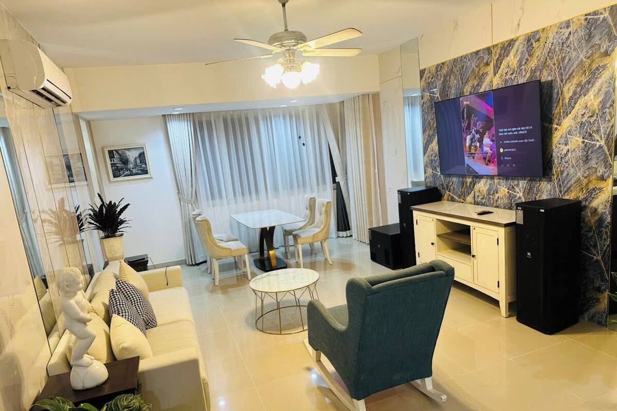 Ein modernes Wohnzimmer mit Sofa, Sessel, Esstisch und Stühlen. Ein Flachbildfernseher ist an der Wand befestigt.