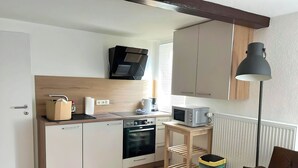 A compact kitchen with a microwave, oven, and a small table with a lamp.