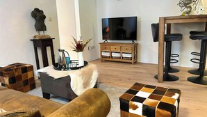 A living room with a sofa, ottoman, TV, wooden cabinet, and bar stools.