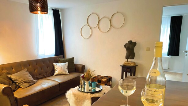A living room with a brown leather sofa, a coffee table, a small side table, and a wine bottle with a glass.
