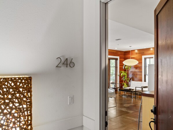 A modern interior with a number '246' on the wall, a glass door, and a view into a well-lit living area with a dining table and chairs.