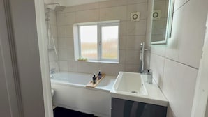 A bathroom with a bathtub, a shower, a sink, and a window. - Manchester Home Away From Home (Manchester)