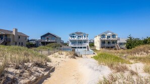 A beachfront property with a sandy path leading to a row of three-story houses with balconies. - 800 Luxury 8BR Oceanfront Retreat w/Pool & Hot Tub (Nags Head)