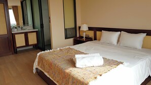 Une chambre d’hôtel avec un grand lit, une table de chevet avec une lampe, un miroir et une salle de bain visible à travers une porte ouverte.