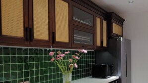 Une cuisine avec des meubles de couleur bois foncé, un plan de travail blanc, un réfrigérateur noir et un crédence en carreaux verts.