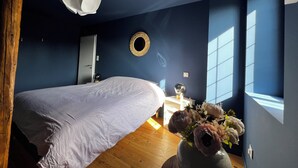 A bedroom with a bed, a round mirror, a vase with flowers, and a window with blinds. - New home! La Buissonnière, 12 to 14 pers with Spa, 45min from Strasbourg. (Erckartswiller)