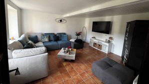 A living room with a sectional sofa, a white armchair, a coffee table, and a TV mounted on the wall. - New home! La Buissonnière, 12 to 14 pers with Spa, 45min from Strasbourg. (Erckartswiller)